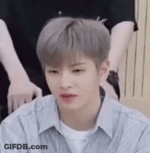 A Young Man With Gray Hair And A White Shirt Is Sitting Down . GIF