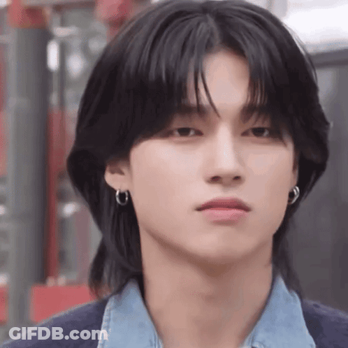 A Young Man With Long Black Hair And Earrings Is Wearing A Denim Shirt And A Blue Cardigan . GIF
