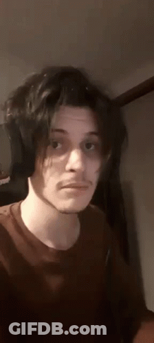 A Young Man With Long Black Hair And Headphones Is Making A Funny Face . GIF