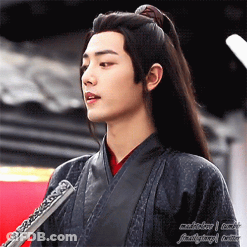 A Young Man With Long Black Hair Is Holding A Flute In His Hand . GIF