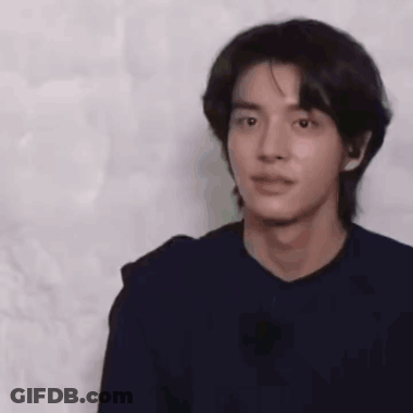 A Young Man With Long Black Hair Is Wearing A Black Shirt And Looking At The Camera . GIF