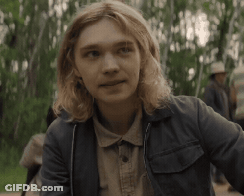 A Young Man With Long Blonde Hair Is Wearing A Denim Jacket GIF
