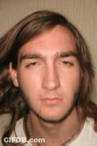 A Young Man With Long Hair And A Necklace Around His Neck Looks At The Camera GIF