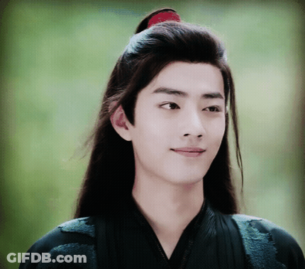 A Young Man With Long Hair And A Red Ponytail Is Smiling GIF