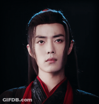 A Young Man With Long Hair And A Red Scarf Around His Neck Looks At The Camera GIF