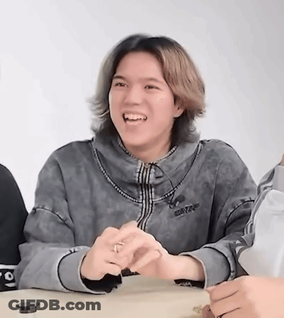 A Young Man With Long Hair Is Sitting At A Table Laughing . GIF
