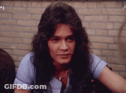 A Young Man With Long Hair Is Sitting In Front Of A Brick Wall And Looking At The Camera . GIF