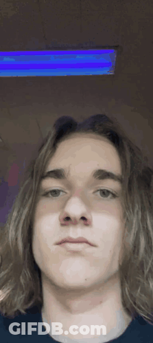 A Young Man With Long Hair Is Taking A Selfie With A Blue Light Behind Him . GIF