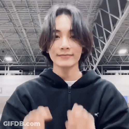 A Young Man With Long Hair Is Wearing A Black Hoodie And Making A Peace Sign . GIF