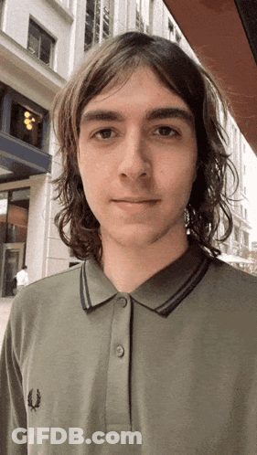 A Young Man With Long Hair Is Wearing A Green Fred Perry Shirt GIF