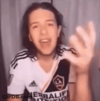 A Young Man With Long Hair Is Wearing A White And Black Adidas Shirt And Waving His Hand . GIF