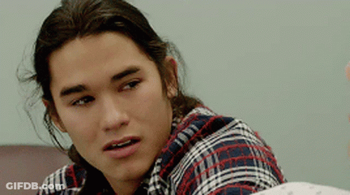 A Young Man With Long Hair Wearing A Plaid Shirt Looks At The Camera GIF