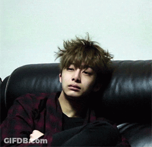 A Young Man With Messy Hair Is Sitting On A Black Couch GIF