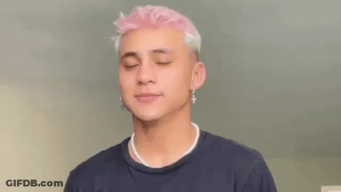 A Young Man With Pink Hair And Pearl Necklace Is Wearing A Black Shirt And Earrings . GIF