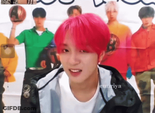 A Young Man With Pink Hair Is Smiling In Front Of A Group Of Men GIF