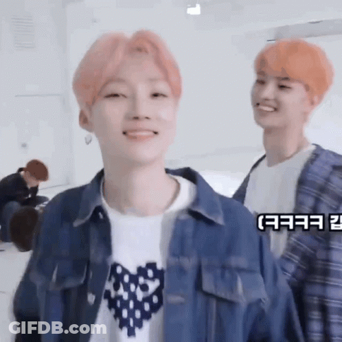 A Young Man With Pink Hair Is Smiling While Standing Next To Another Young Man With Orange Hair . GIF
