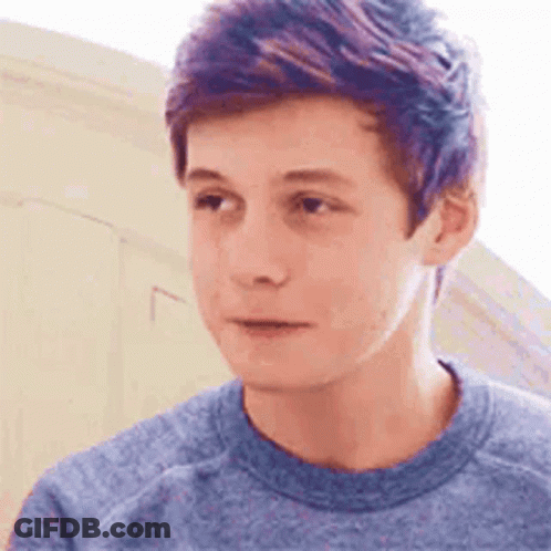 A Young Man With Purple Hair Is Wearing A Blue Shirt And Looking At The Camera . GIF