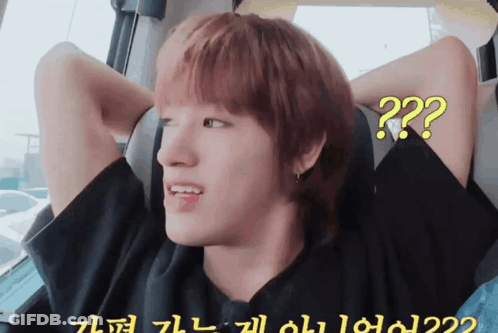 A Young Man With Red Hair Is Sitting In A Car With His Hands Behind His Head And A Question Mark On His Face GIF