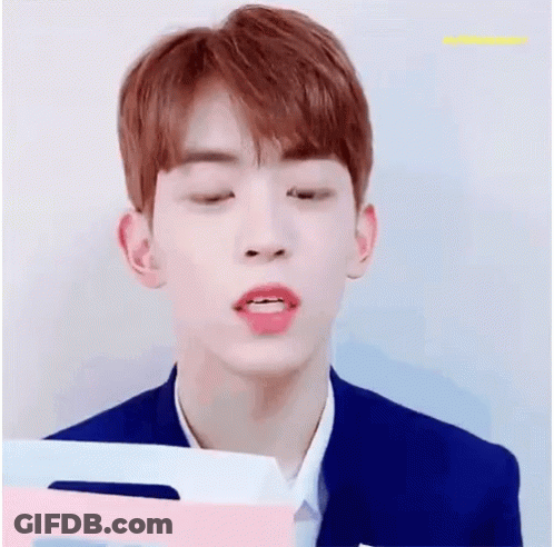 A Young Man With Red Hair Is Smiling While Holding A Pink And Blue Folder . GIF