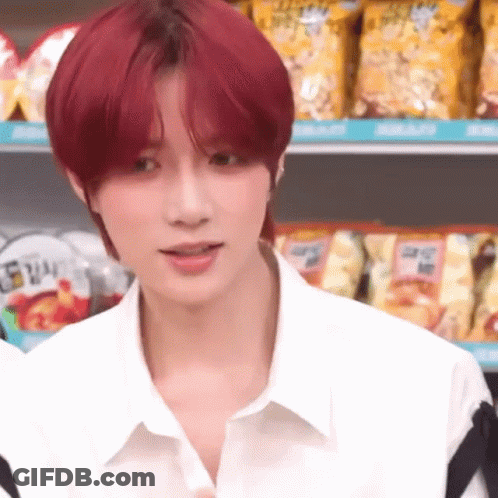 A Young Man With Red Hair Is Wearing A White Shirt And Standing In Front Of A Shelf Of Chips . GIF