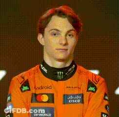 A Young Man With Red Hair Is Wearing An Orange Racing Suit And Looking At The Camera . GIF