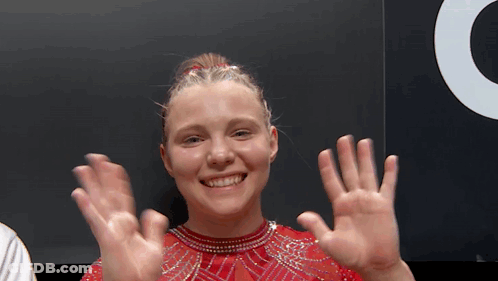A Young Woman In A Red Dress Is Smiling And Waving Her Hands . GIF
