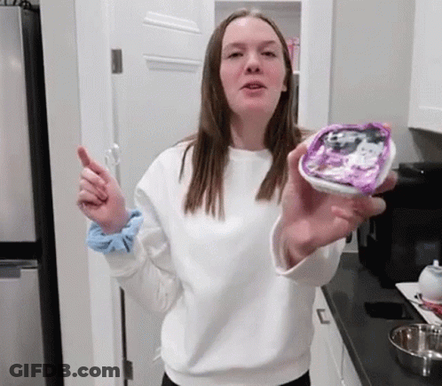 A Young Woman In A White Sweater Is Holding A Container Of Food In Her Hand . GIF