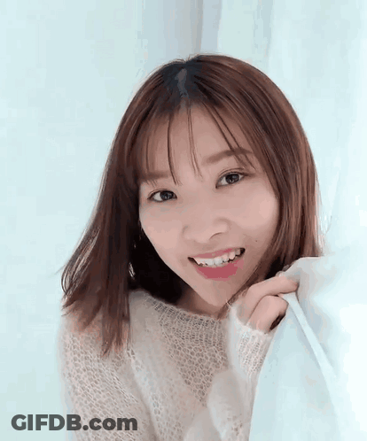 A Young Woman In A White Sweater Is Smiling While Holding A Blue Curtain . GIF