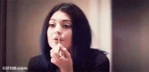 A Young Woman Is Applying Lipstick In Front Of A Mirror . GIF