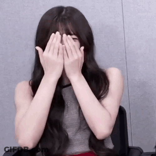 A Young Woman Is Covering Her Face With Her Hands While Sitting In A Chair . GIF