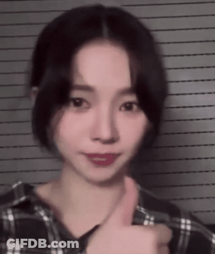 A Young Woman Is Giving A Thumbs Up Sign While Wearing A Plaid Shirt . GIF