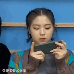 A Young Woman Is Holding A Cell Phone In Her Hands . GIF