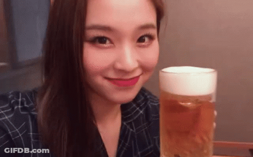 A Young Woman Is Holding A Glass Of Beer And Smiling . GIF