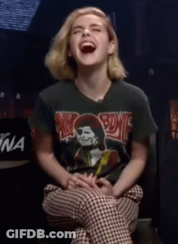 A Young Woman Is Laughing While Wearing A Black Shirt With A Picture Of A Skull On It . GIF
