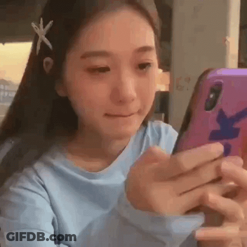 A Young Woman Is Looking At Her Cell Phone While Wearing A Blue Shirt . GIF
