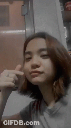 A Young Woman Is Making A Funny Face And Giving A Thumbs Up Sign . GIF