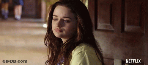A Young Woman Is Sitting In Front Of A Door Looking At The Camera . GIF