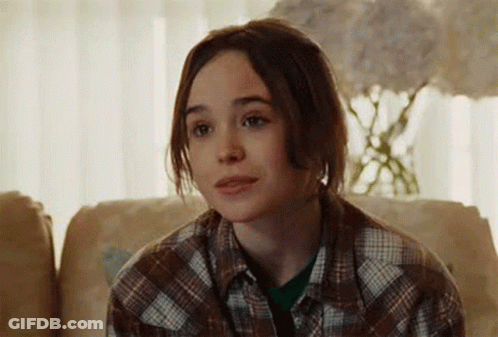A Young Woman Is Sitting On A Couch Wearing A Plaid Shirt And Looking At The Camera . GIF
