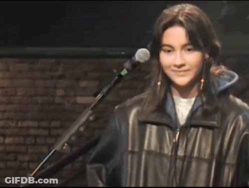 A Young Woman Is Smiling In Front Of A Microphone In A Dark Room . GIF
