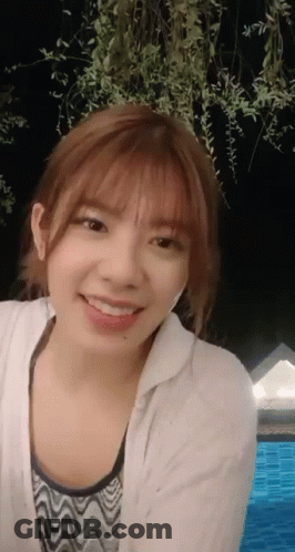 A Young Woman Is Smiling In Front Of A Pool At Night GIF