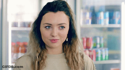 A Young Woman Is Standing In Front Of A Vending Machine Filled With Sodas . GIF