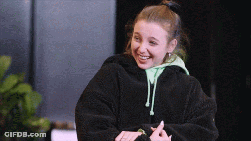 A Young Woman Wearing A Black Jacket And A Green Hoodie Smiles GIF