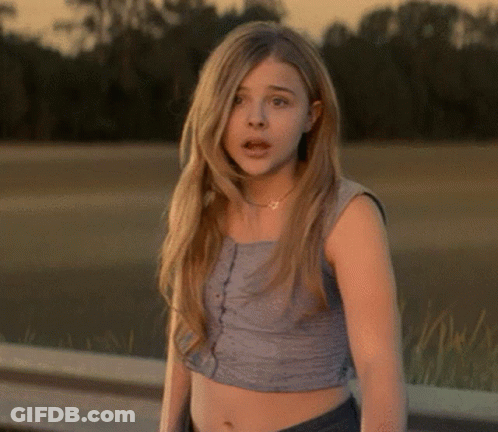 A Young Woman Wearing A Crop Top Stands In Front Of A Body Of Water GIF