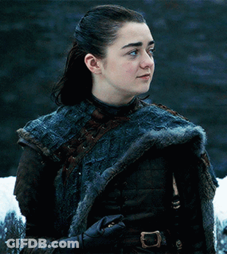 A Young Woman Wearing A Fur Coat And Gloves Is Standing In Front Of A Waterfall . GIF