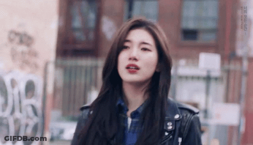 A Young Woman Wearing A Leather Jacket And A Plaid Shirt Is Standing In Front Of A Building . GIF