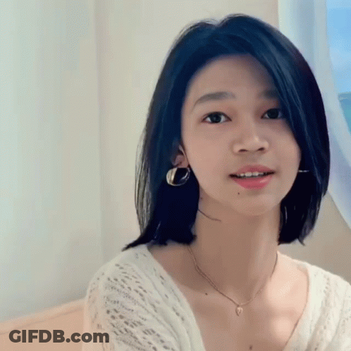 A Young Woman Wearing A Necklace And Earrings Is Smiling GIF