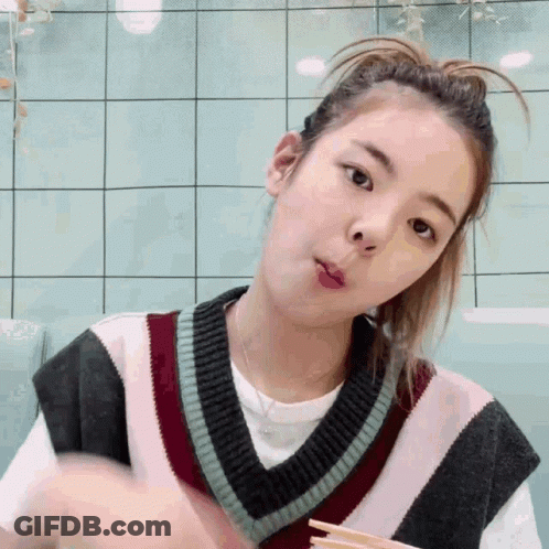 A Young Woman Wearing A Sweater Vest And A Ponytail Is Eating With Chopsticks . GIF