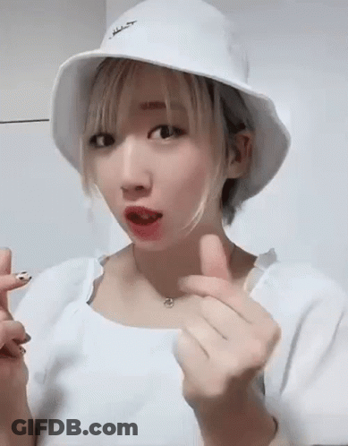 A Young Woman Wearing A White Hat And A White Shirt Is Making A Heart Shape With Her Hands . GIF