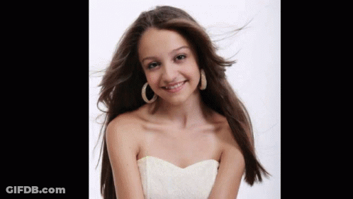A Young Woman Wearing A White Strapless Dress And Hoop Earrings Smiles GIF