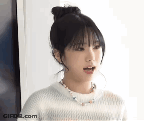 A Young Woman Wearing A White Sweater And A Necklace Is Making A Surprised Face . GIF